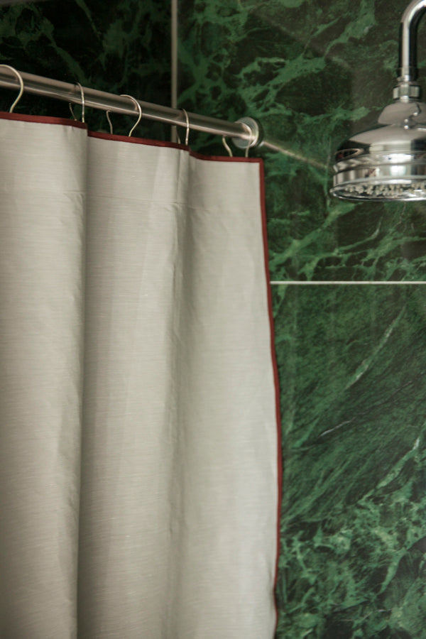 Winther Wackerhausen Clean shower curtain with Deep Reddish Brown trim hanging in a bathroom with rich green marble tiles and chrome shower fittings.