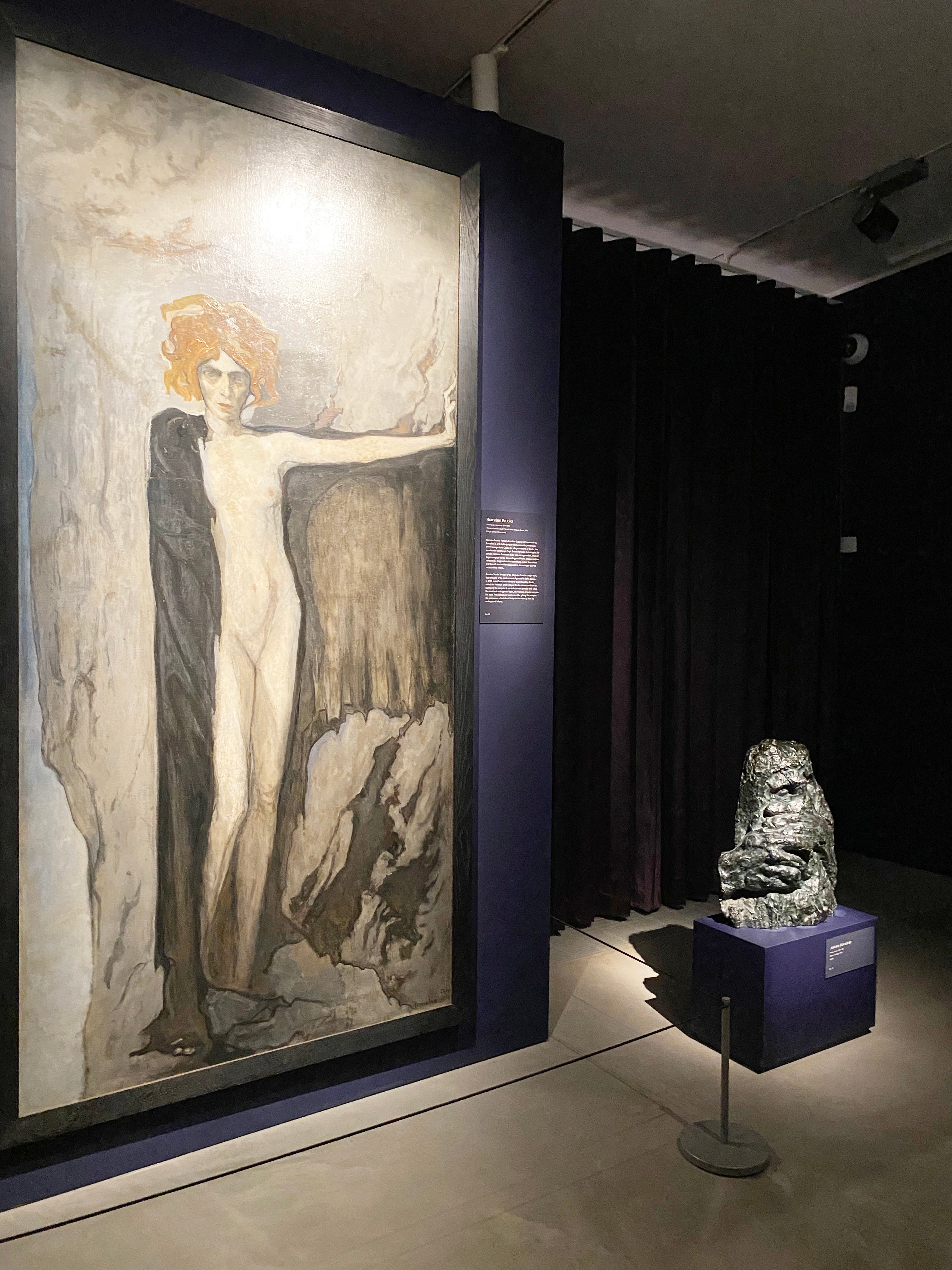 Udstillingsscene på Ordrupgaard med monumentalt maleri af kvindefigur flankeret af mørke gardiner og skulptur i front.