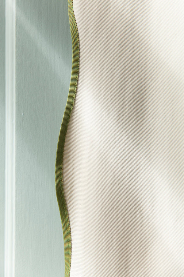 Detail shot of the Wave shower curtain by Winther Wackerhausen, highlighting the sculptural wavy edge and green trim against a soft, minimal bathroom background.